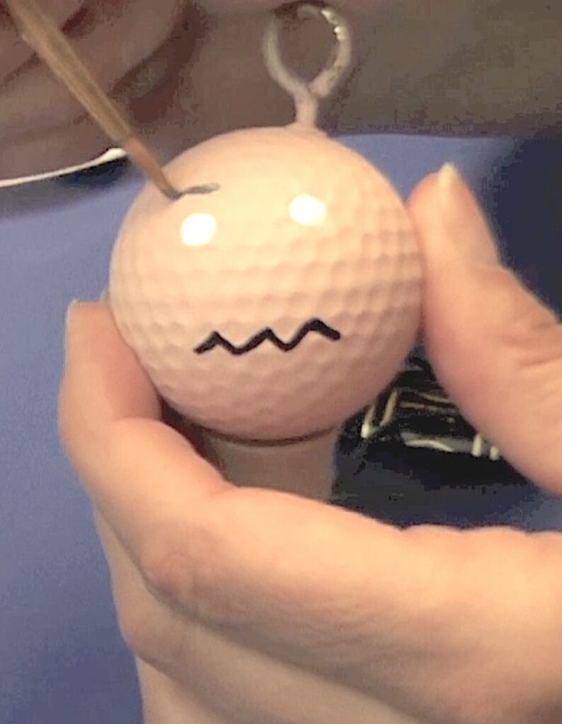 Paint eyebrows onto flesh golf ball with a small paintbrush