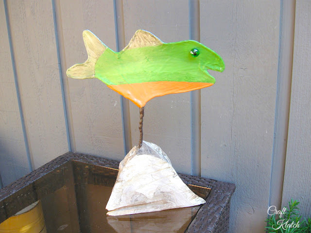 Orange and green fish sculpture with a natural wood base