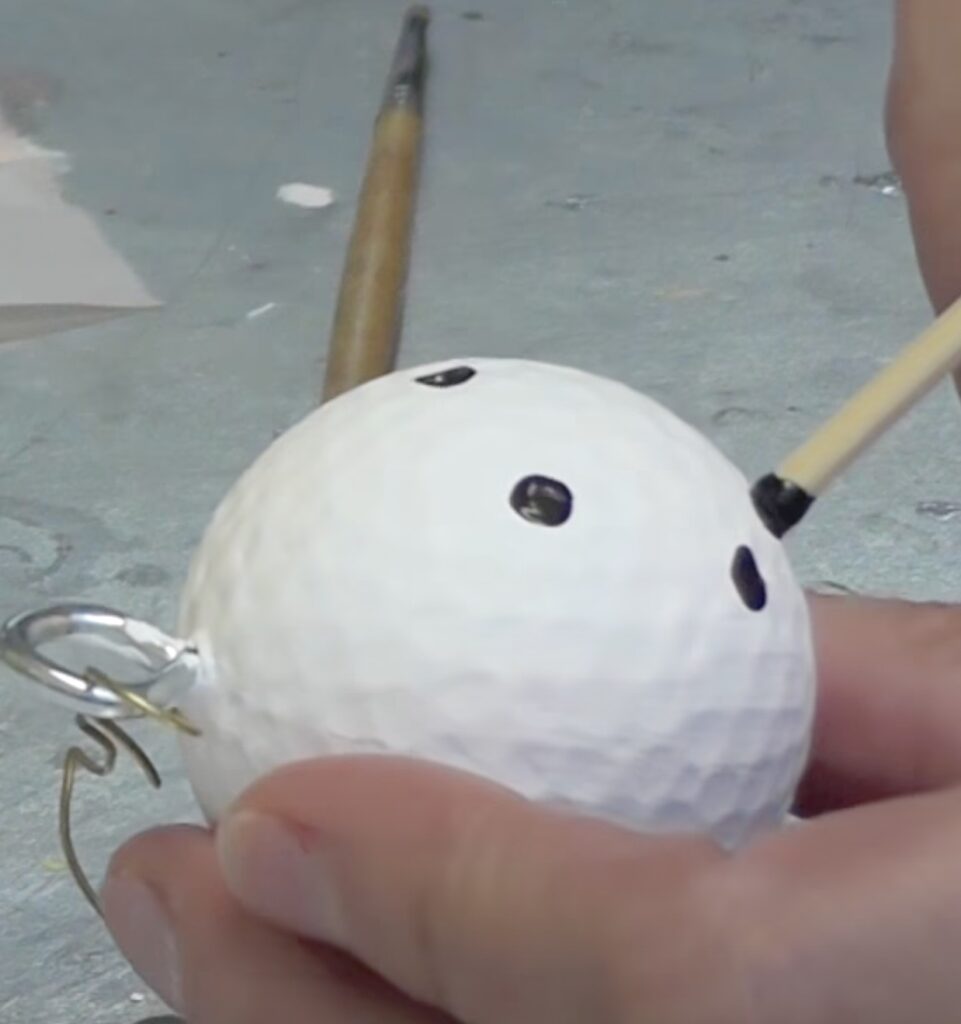 Use a skewer stick dipped in black paint to add snowman eyes and mouth to the golf ball