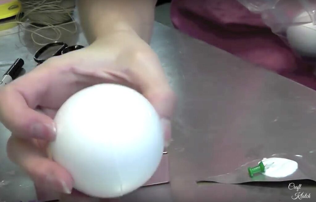 Holding styrofoam ball and pushpin dipped in glue