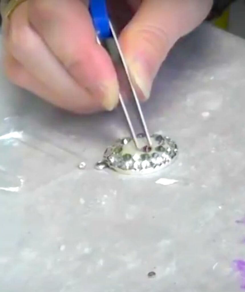 Using tweezers to carefully add swarovski crystals to the epoxy clay jewelry piece