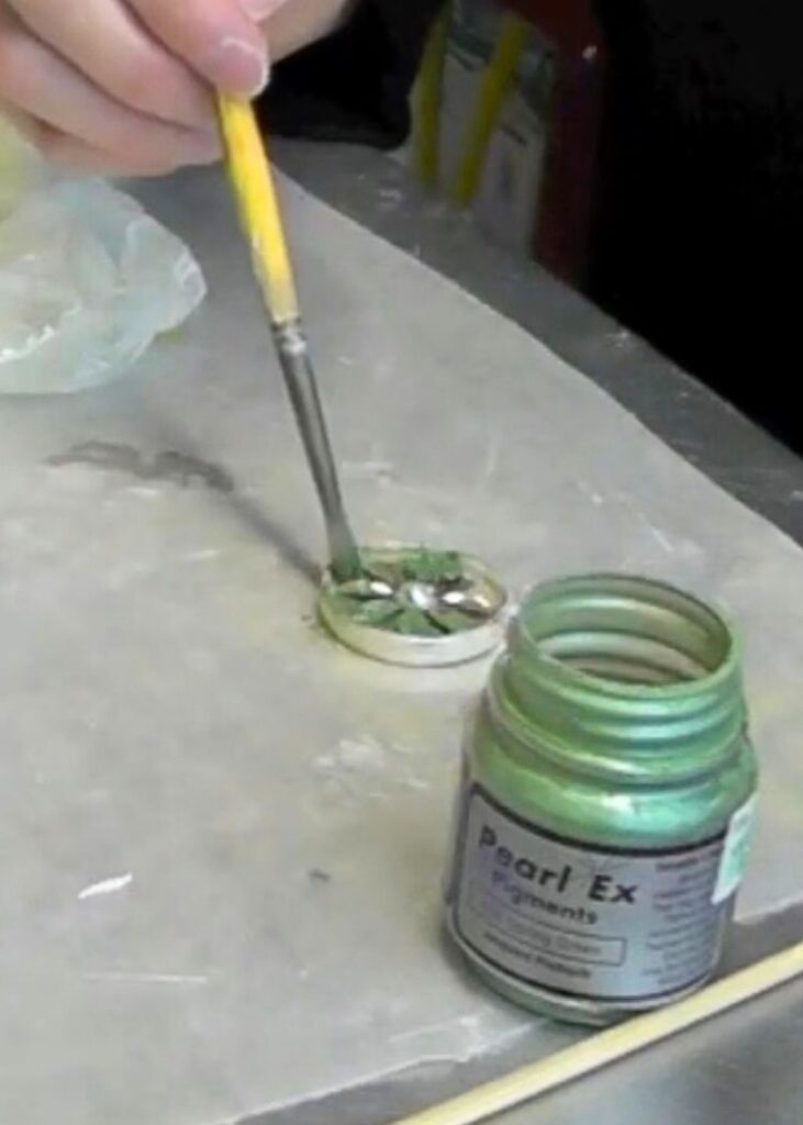 Brushing green pigment powder on the epoxy clay and flower in the bezel while showing how to make metal jewelry