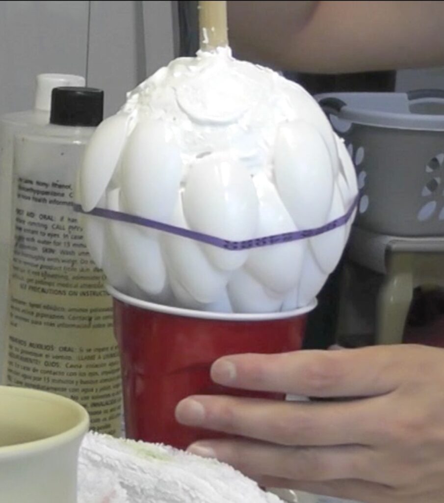 Styrofoam ball with the artichoke leaves upside down in a cup and a rubber band