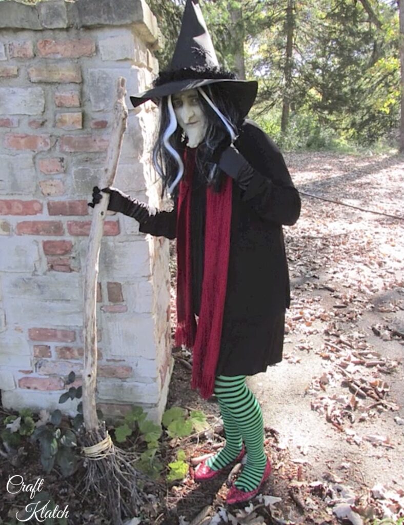 Witch Halloween costume with red scarf, green striped tights and a broomstick