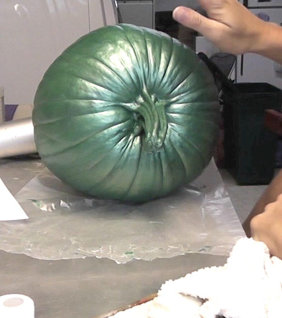 Metallic green painted pumpkin laying on its side