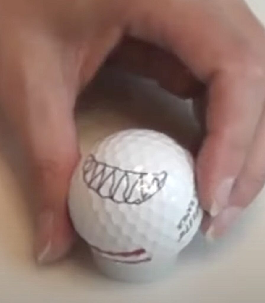 Golf ball with shark face drawn on it