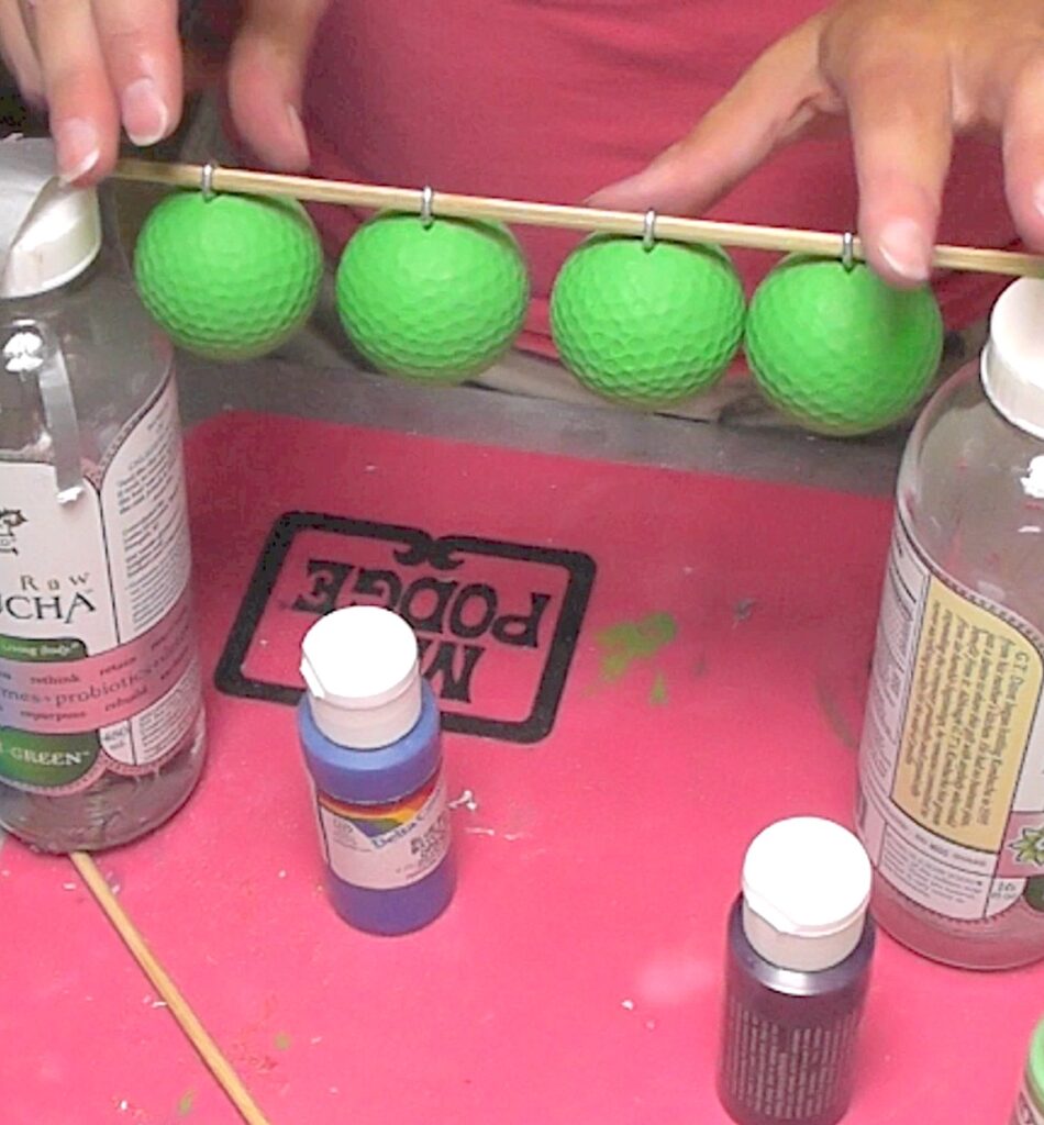 Four green painted golf balls hanging from skewer