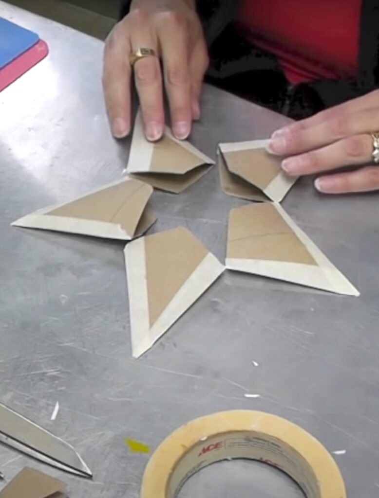 Using masking tape to tape the point of the toilet paper Christmas stars together