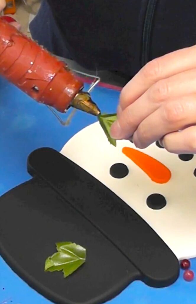 Putting hot glue on a fake leaf to put on the big snowman decoration
