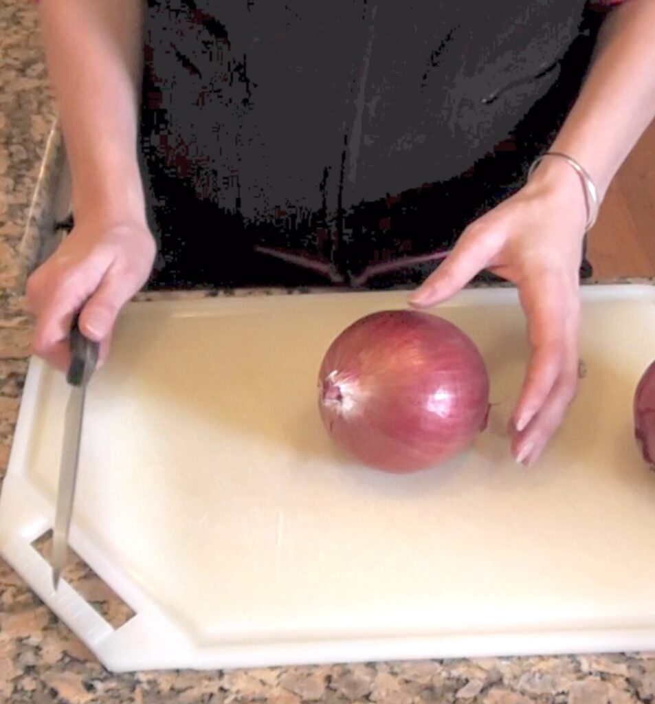 Knife in right hand ready to cut red onion on cutting board