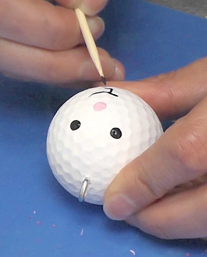 Paint bunny face onto golf ball with skewer stick