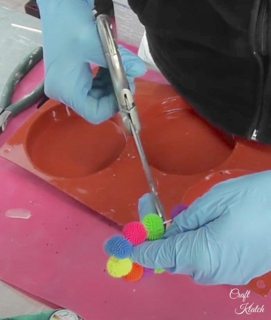 Using scissors to cut elastic holding colorful koosh ball bracelet for splash of color resin diy