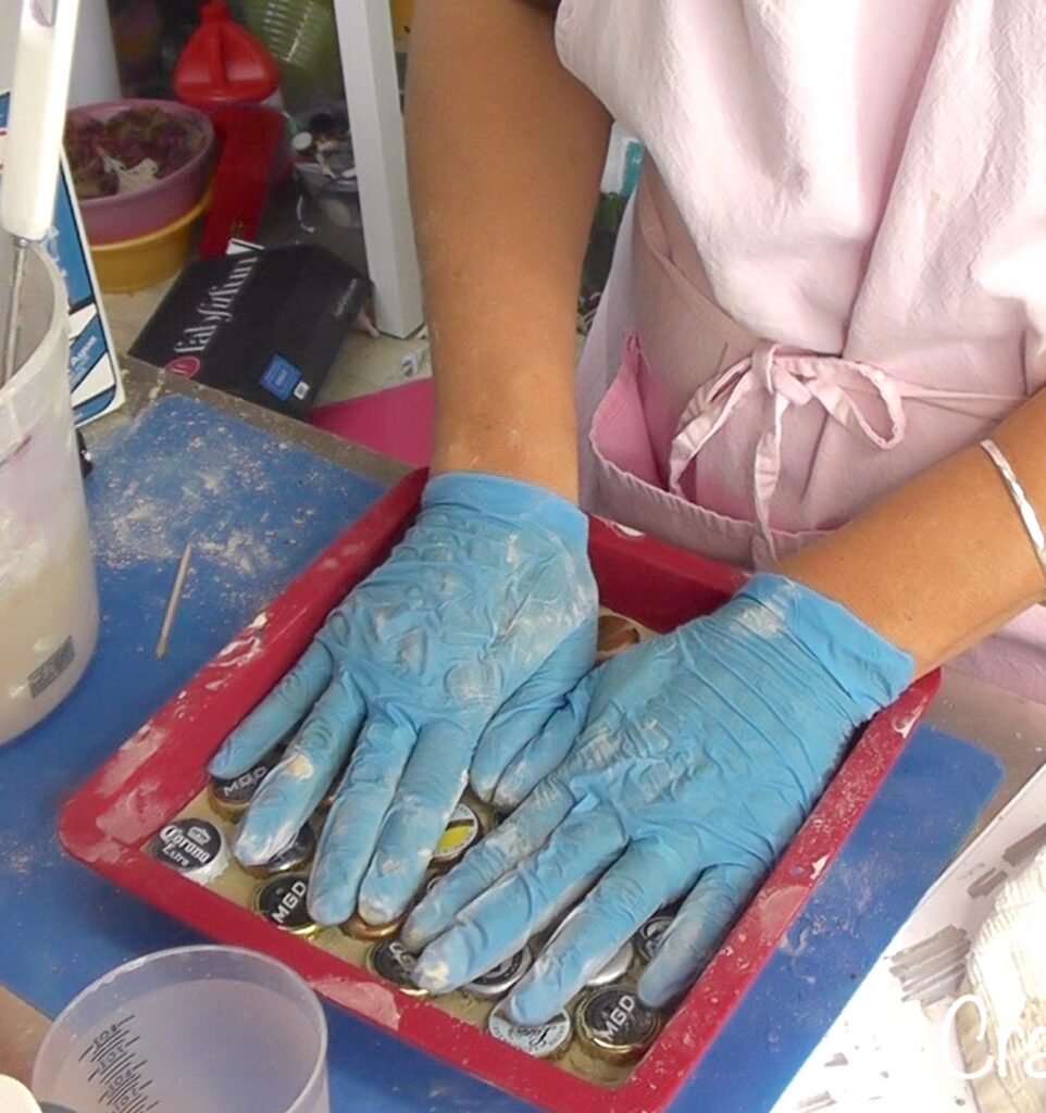 With gloved hands pressing beer bottle caps into the concrete