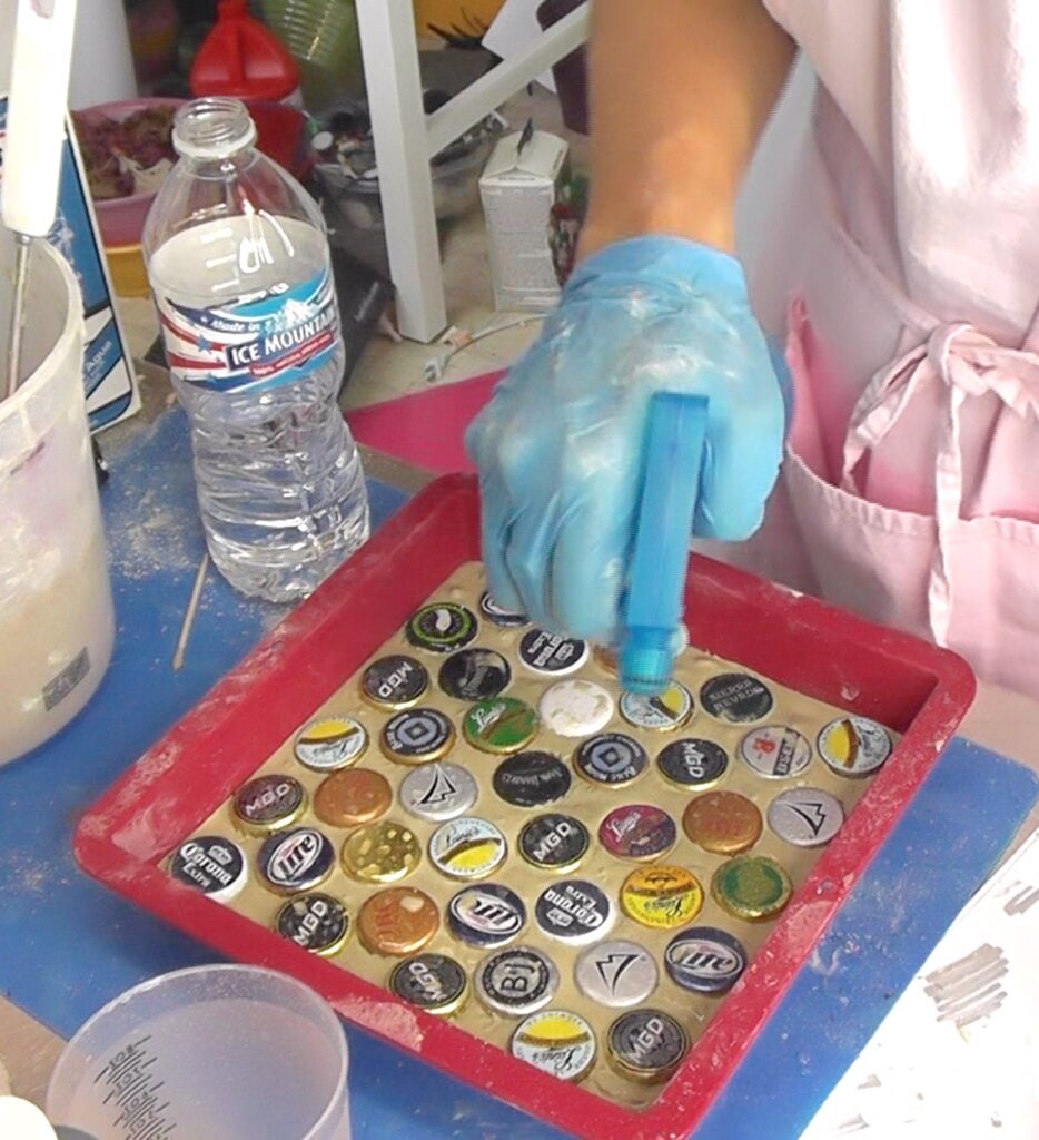 Using spray bottle to moisten concrete with beer bottle caps embedded