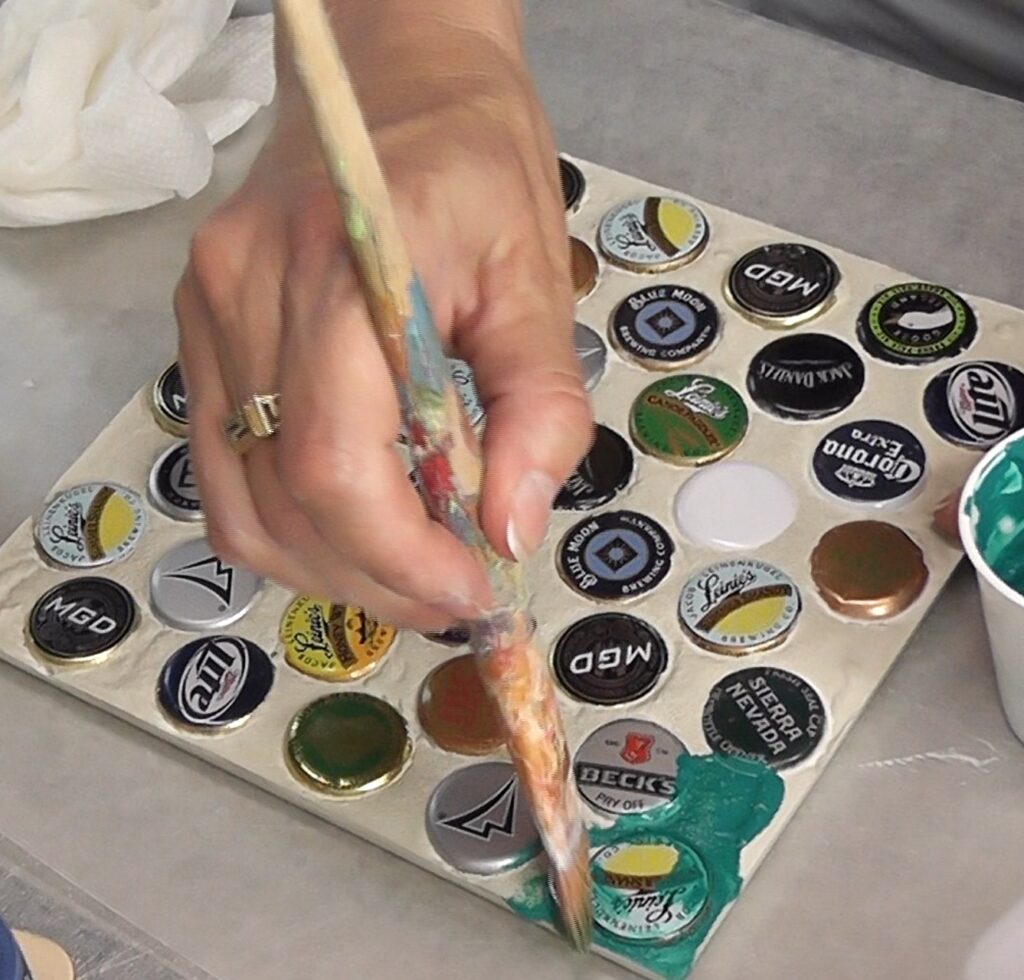 Painting beer bottle cap trivet with a greenish teal paint