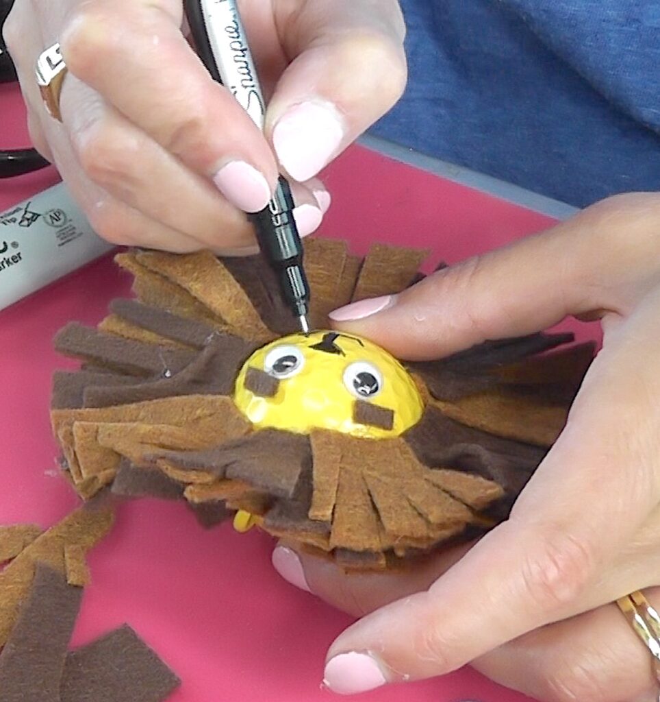 Draw whiskers onto golf ball lion with permanent marker