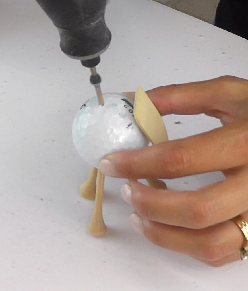 Drill hole into top of golf ball with golf ball tees for legs and tag for face