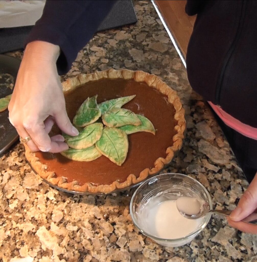 Placing green dough leaves on pumpkin pie