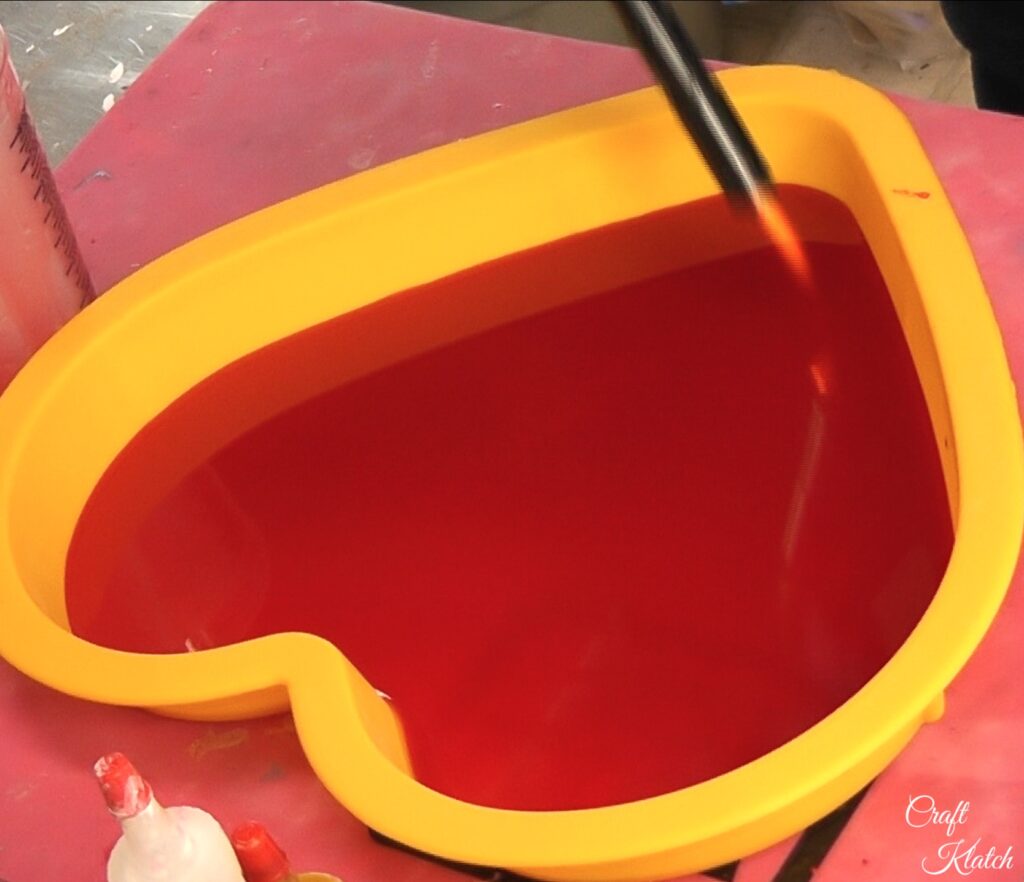 Use lighter to pop bubbles in red heart resin