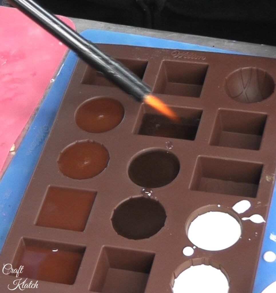 Use lighter to pop bubbles in resin in chocolate mold