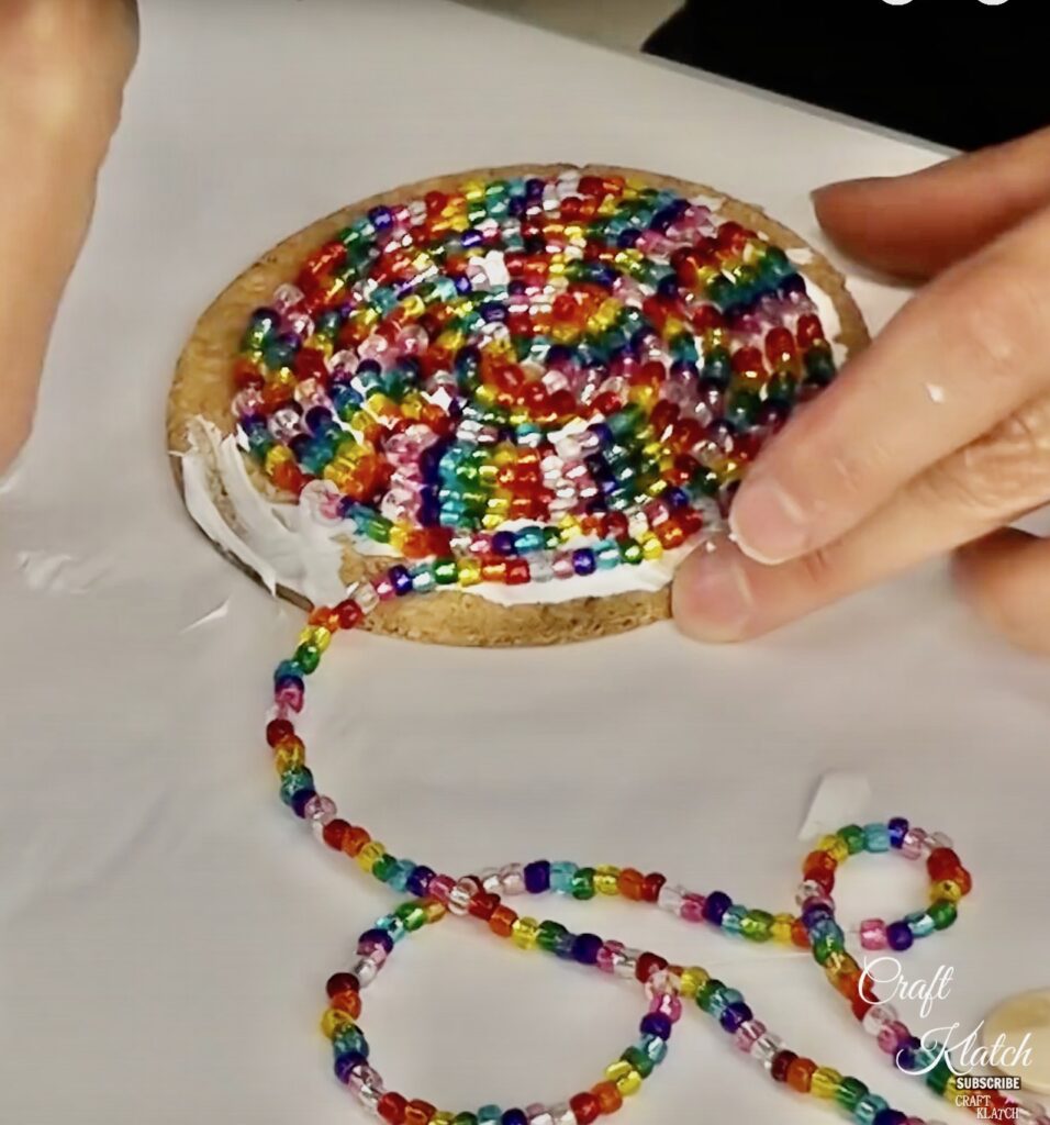 Showing how to make beaded coasters by spiraling colorful glass beads around on a cork round