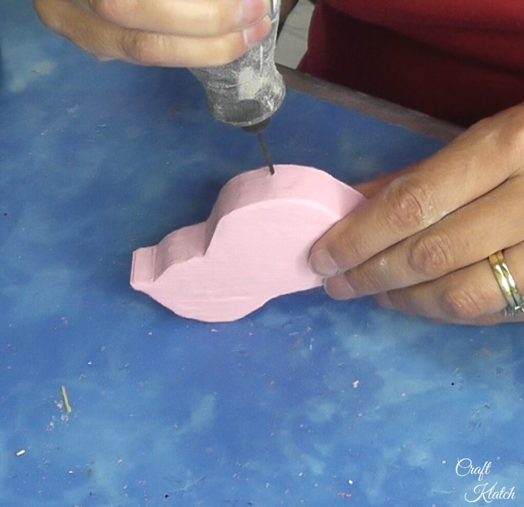 Drilling holes into the bottom of a pink wood bird