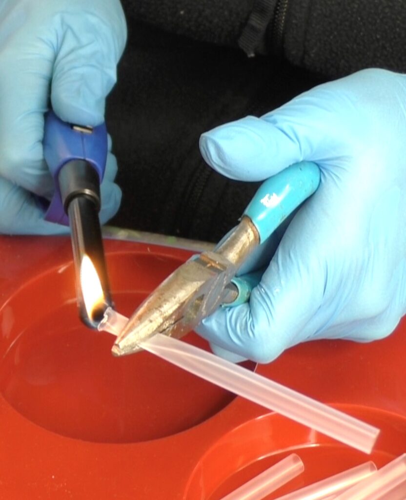 Using pliers to pinch end of straw and melt with a lighter