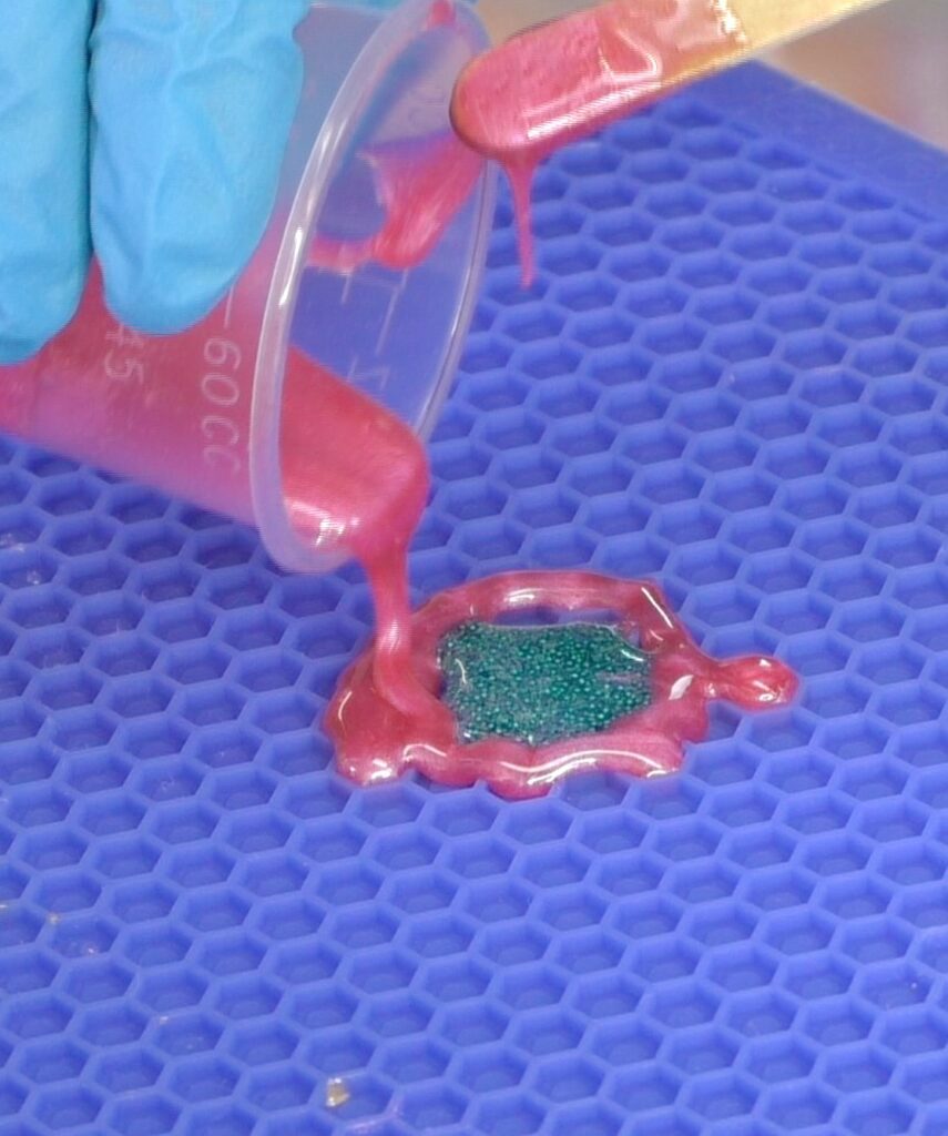Pour blue microbeads mixed with resin and pink resin onto honeycomb silicone mat for freeform coaster