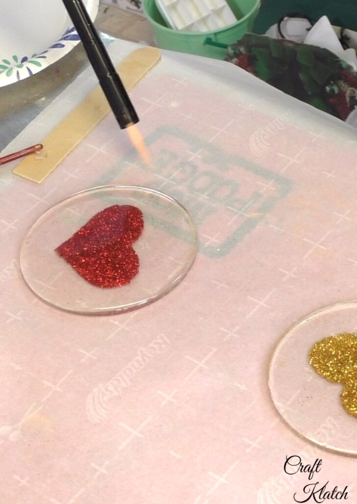 Use lighter to pop bubbles on glitter heart coasters