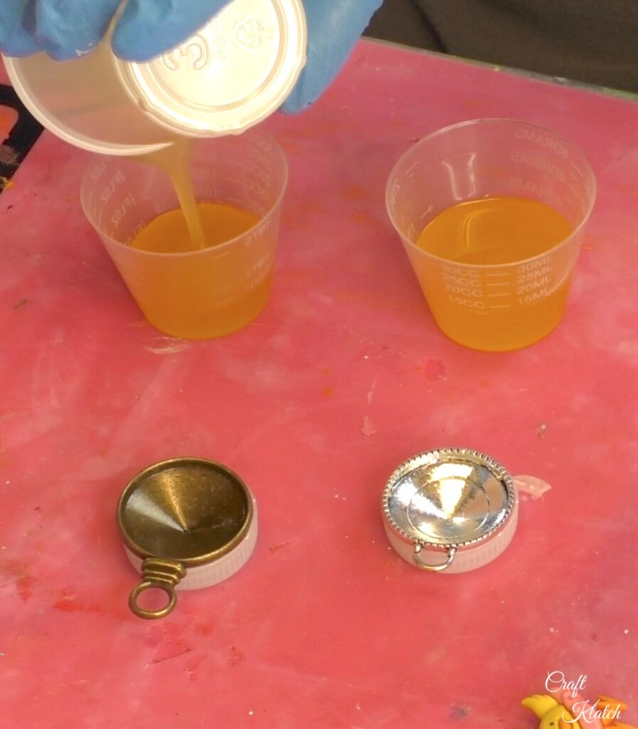 Pouring resin into a cup with silver and bronze bezels placed on plastic bottle caps
