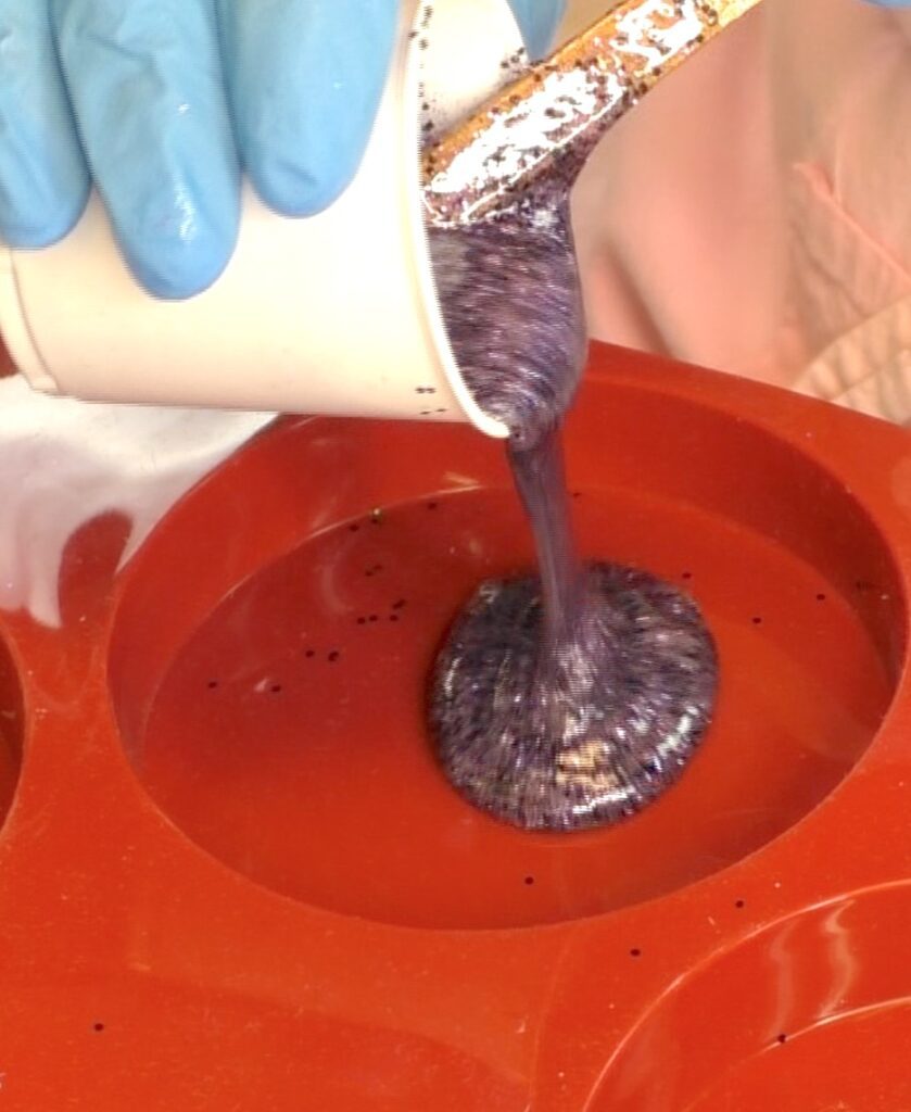 Pouring purple and black resin glitter into coaster mold for the halloween bat craft