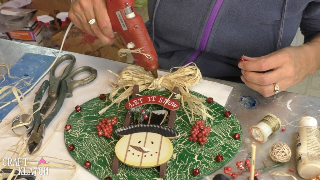 I found this ornament at Dollar Tree, in fact I found four! I decided I would style the ornament four different ways! This is the first and I'm going for a Rustic Snowman Christmas Ornament DIY! Dollar store crafts are a great way to decorate on a budget and customize your Christmas decorations to reflect your personal style and home decor ideas! #craftklatch #holidaydecorations #dollartree #dollartreecrafts #christmas #christmascraft #christmascraftideas #diy #craft #crafts #crafting #craftideas #howto #christmasdecor, Adding hot glue to the middle of the raffia bow