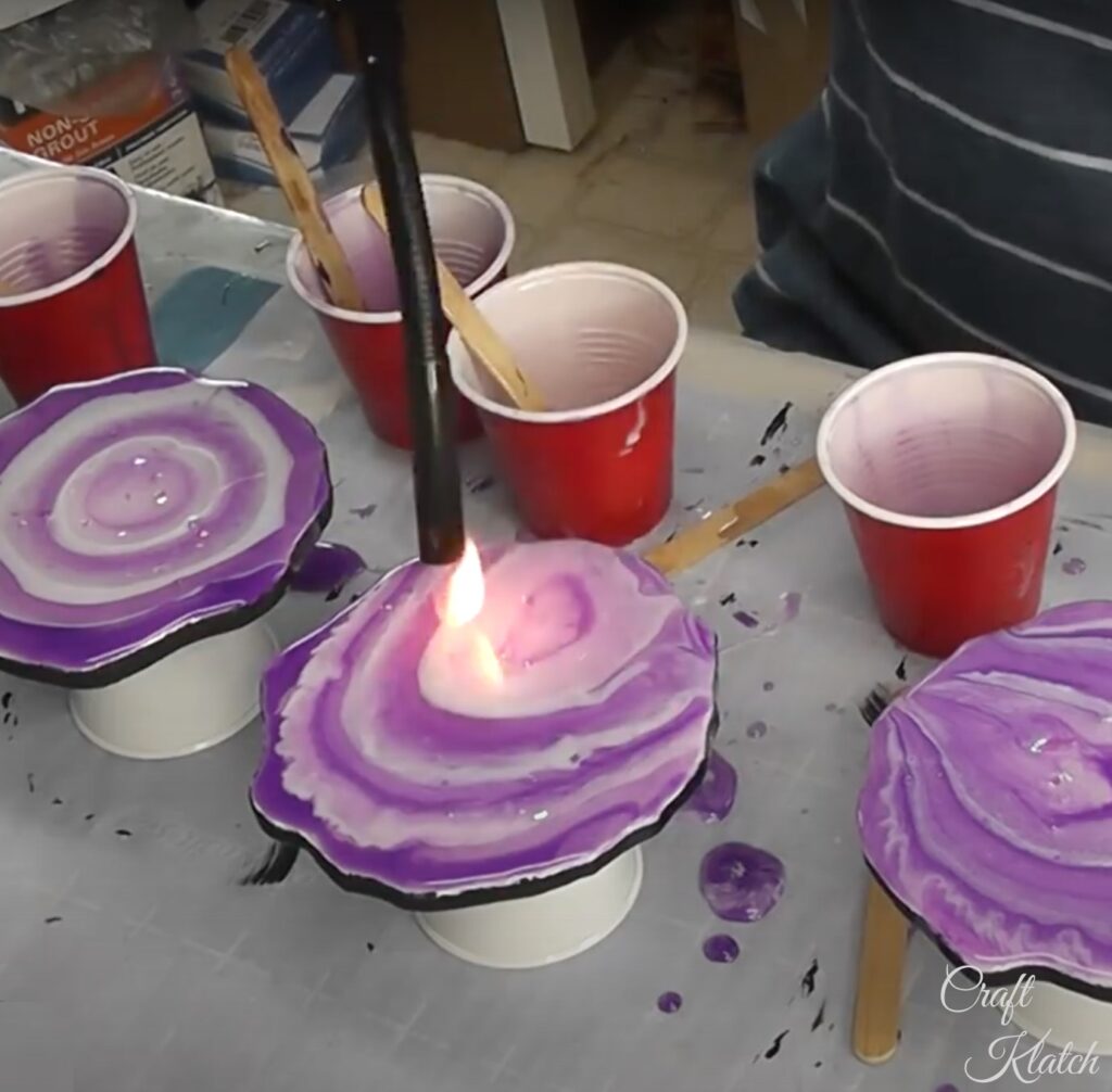 Using a lighter to pop bubbles on purple and white resin geode coasters