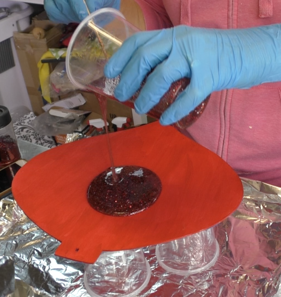 Pouring red glitter resin mixture over Dollar Tree ornament