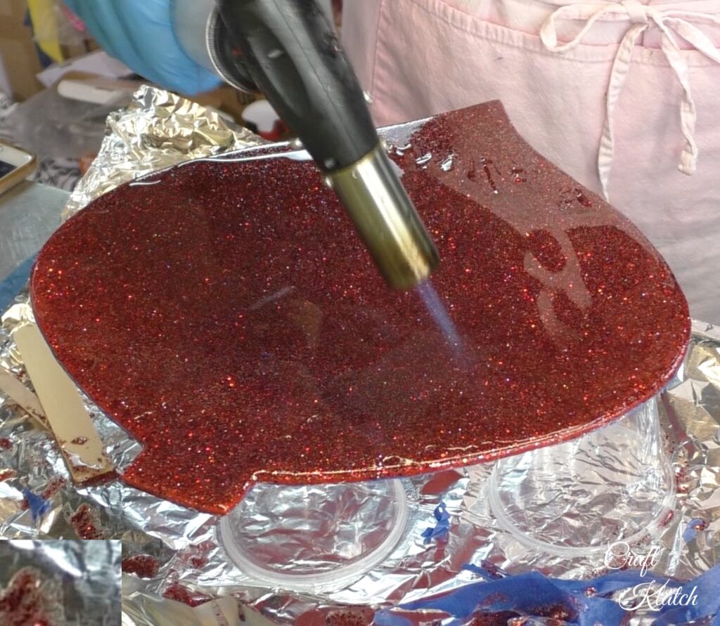 Dollar Tree Ornament Makeover #2 and this time we added glitz and glam to the Christmas decoration tutorial! A little resin and glitter make holiday art! Fun Christmas craft ideas! #craftklatch #craftideas #chiristmas #christmascrafts #resin #resinart #dollartree #dollartreecrafts #dollartreediys Using torch to pop bubbles in resin on Dollar Tree ornament