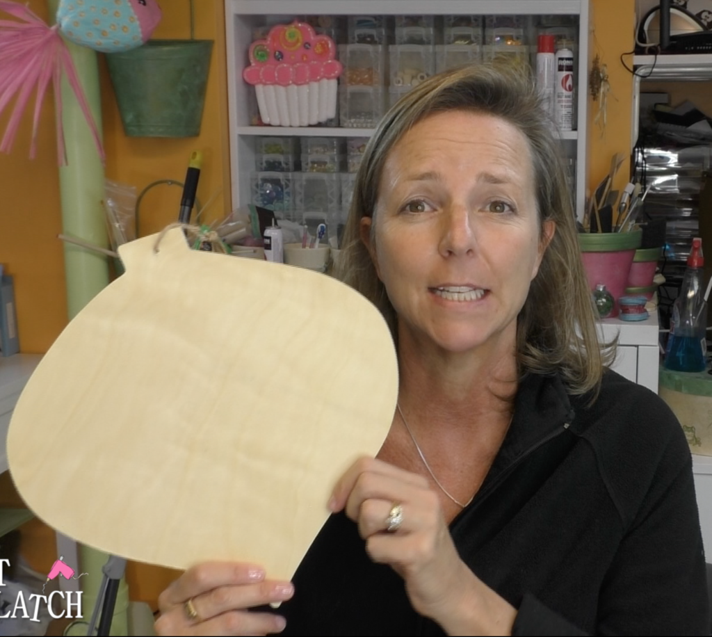 Woman holding up a large, unfinished wood ornament