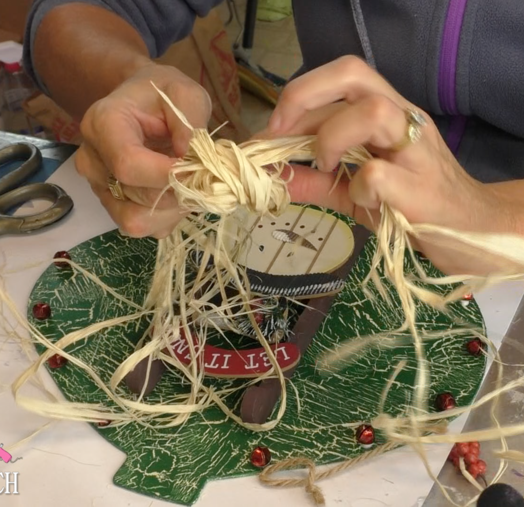 Tying a raffia bow with Christmas ornament in the background