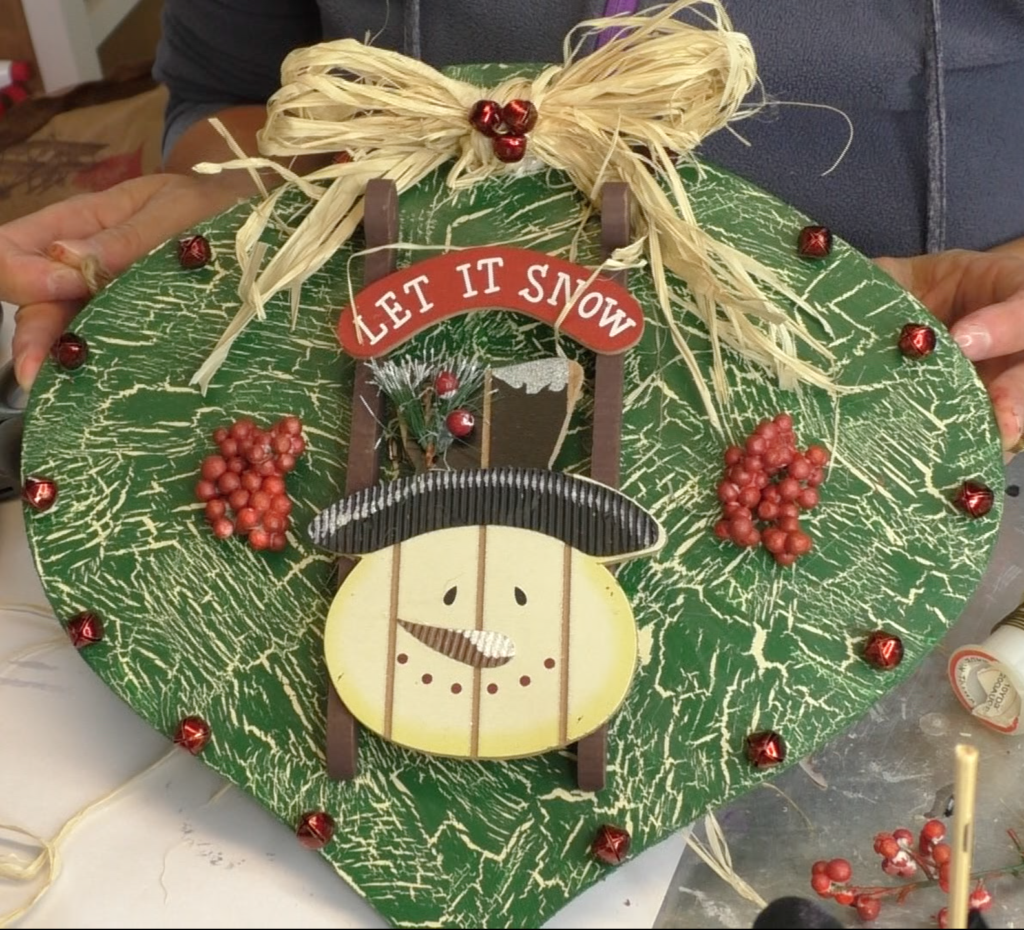 Finished Christmas ornament with snowman sled, red jingle bells, red berries and raffia bow