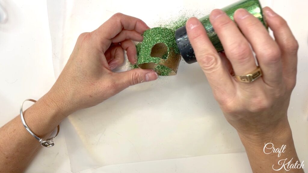 Sprinkle toilet paper roll with green glitter to make the Christmas ornament