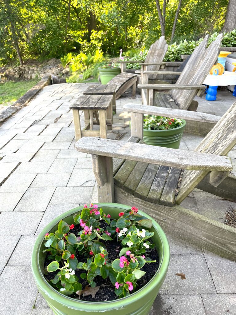 Red, white and pink begonias in a green pot on patio with adironack chairs