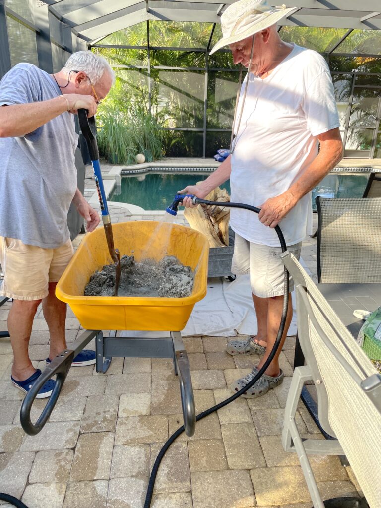 Dad and Greg mixing and wetting concrete with a hose in a yellow wheelbarrow