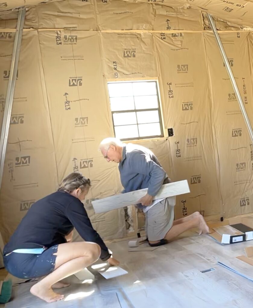 Mona and Dad laying vinyl plank flooring in the shed building