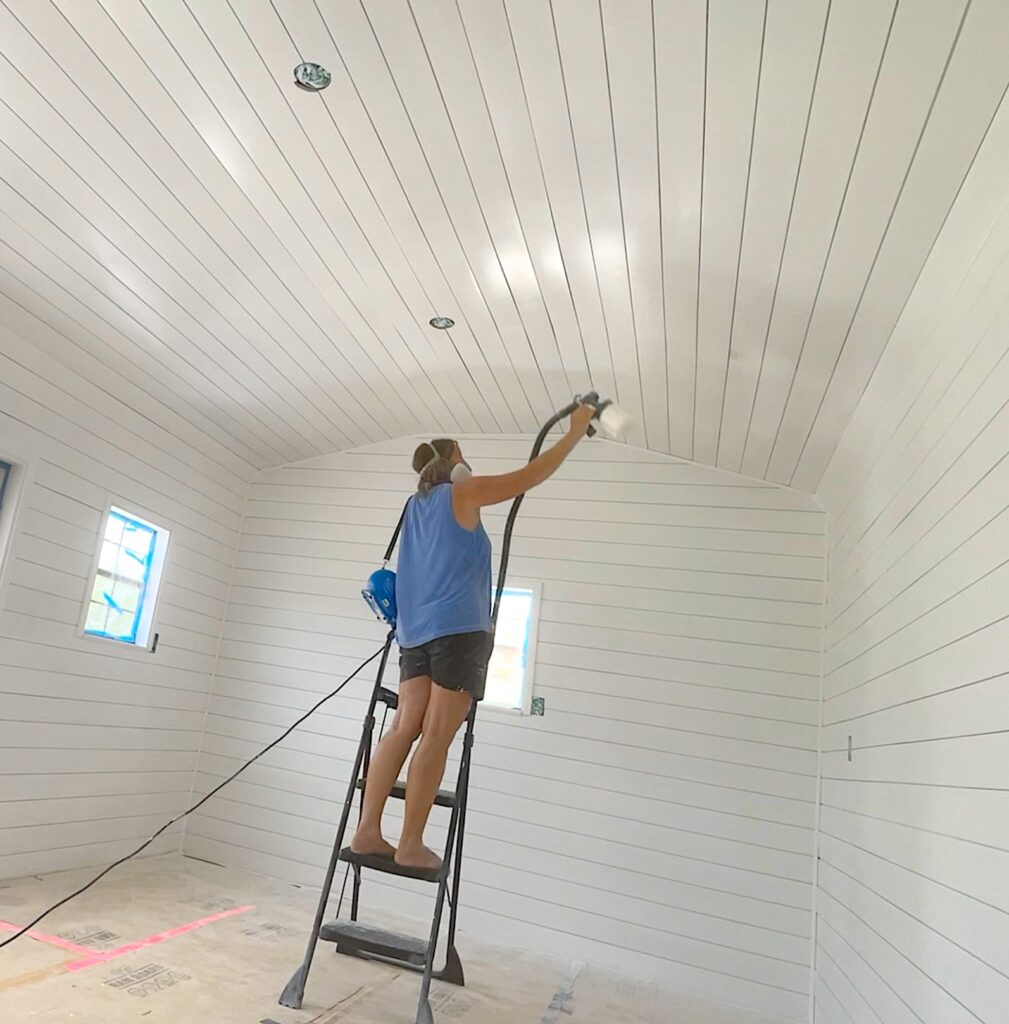Mona using paint sprayer to paint inside of he craft room she shed building and shiplap white