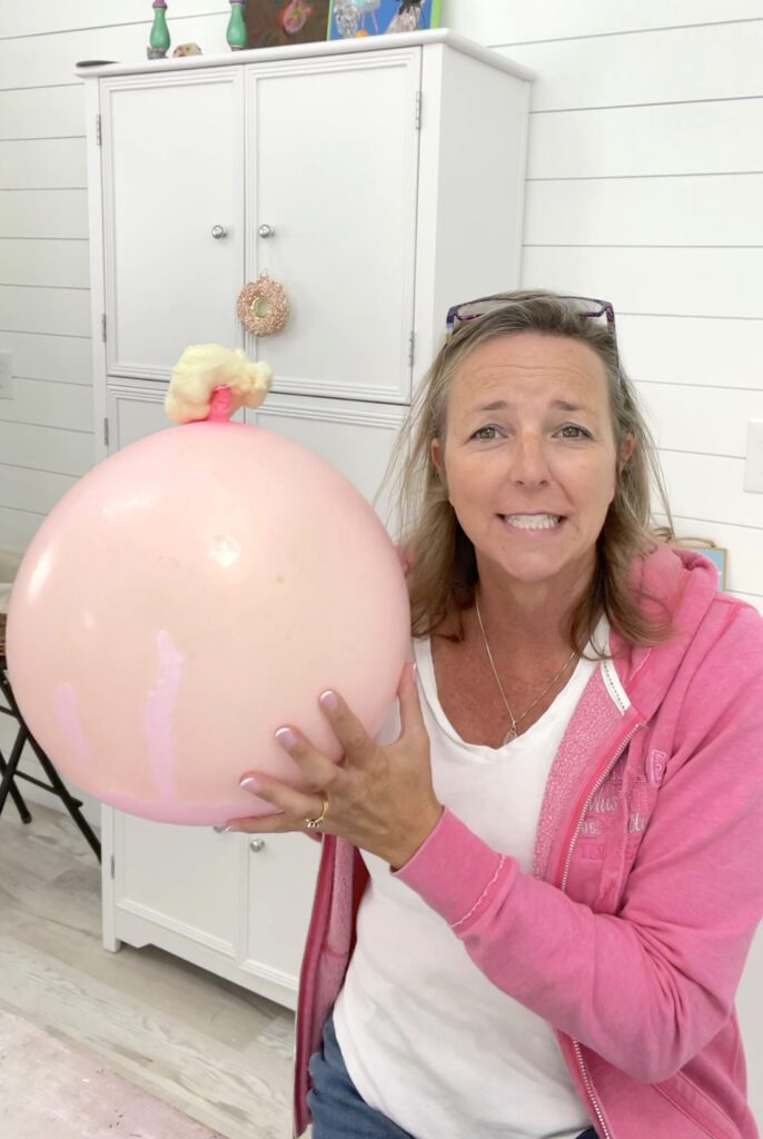 Mona holding pink ballon filled with spray foam oozing out of top of balloon