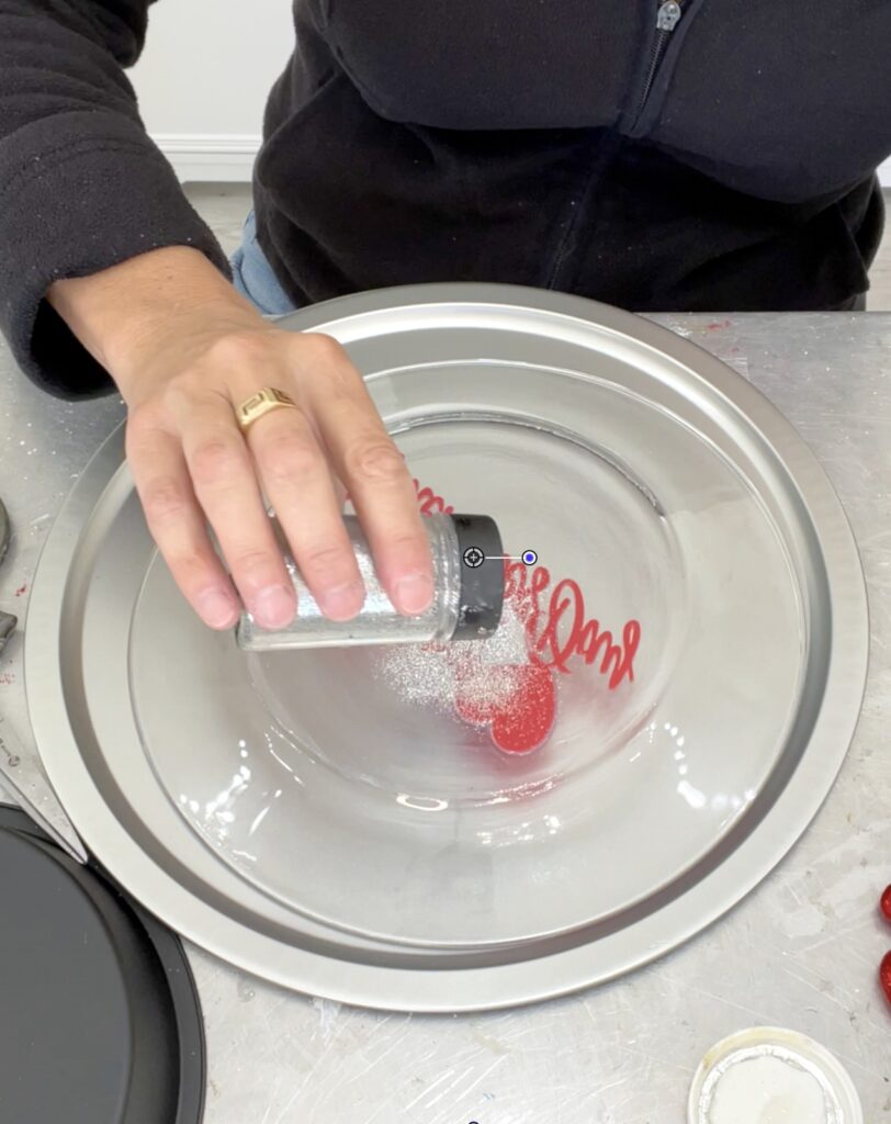 Sprinkling silver glitter on the Valentine dessert platter dollar tree craft