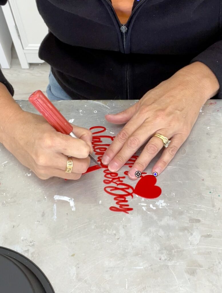 Using craft knife to score the plastic of the Valentines cake topper to remove stem