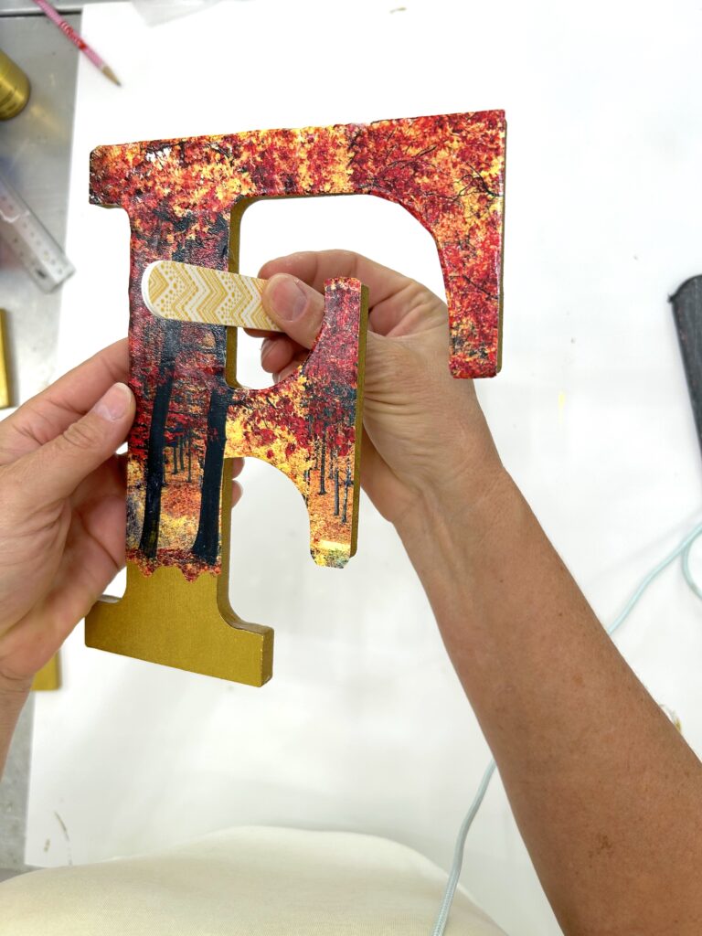 Using an emery board to sand the edges of the decoupaged wood letters for a crisp edge