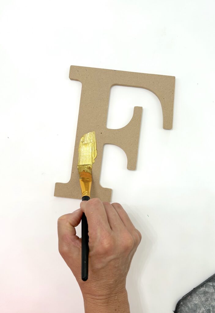 Wood letters being painted with Plaid gold paint