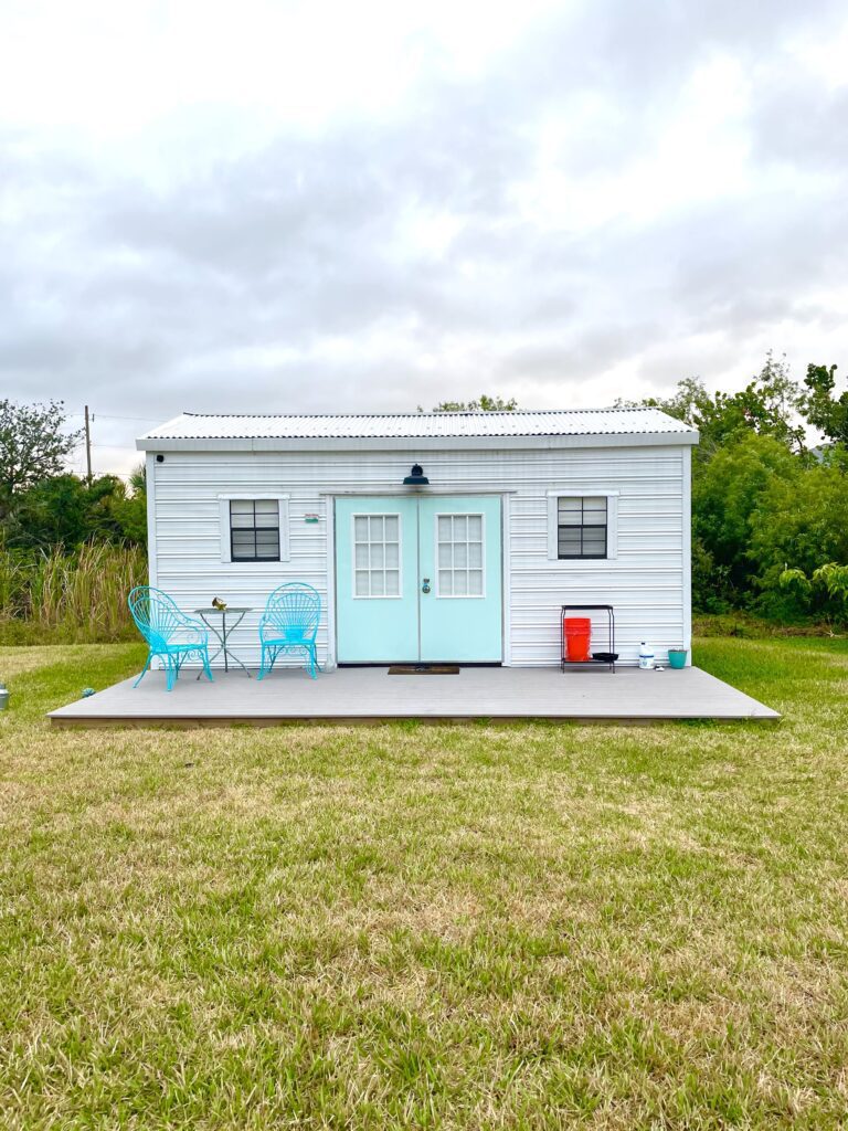 Exterior of craft shed with aqua door, a bistro set and a deck