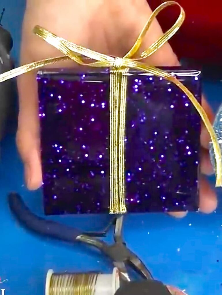 Finished homemade Christmas present made out of resin, chunky purple glitter and a gold ribbon